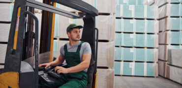 Young worker in unifrom sits in the forklift in the warehouse.